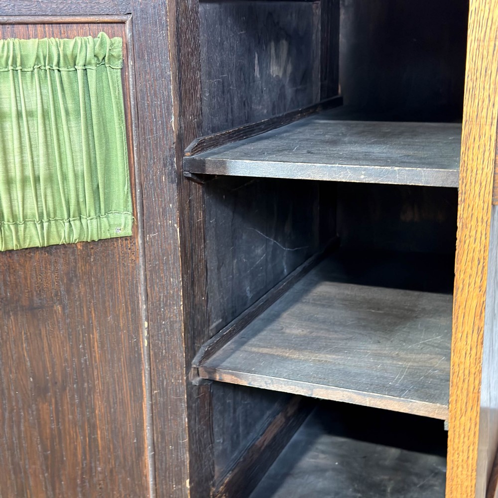 An Arts and Crafts solid oak kneehole desk featuring a raised top gallery shelf, central drawer with geometric moulding, drop handles, and side cupboards with circular gridded glass panels. View VIII