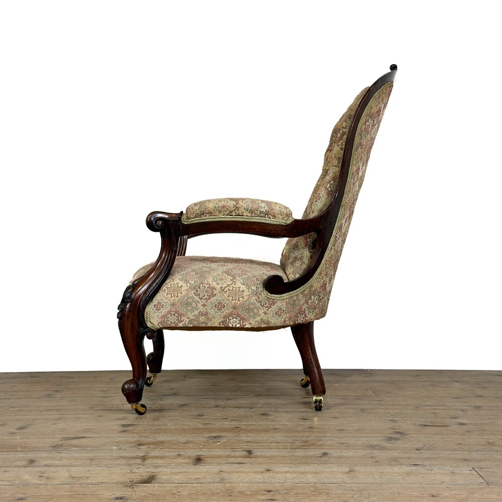 Victorian carved mahogany armchair with deep button-backed floral tapestry upholstery, curved armrests, and cabriole legs on brass castors. View IV