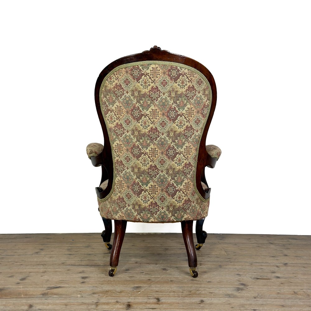 Victorian carved mahogany armchair with deep button-backed floral tapestry upholstery, curved armrests, and cabriole legs on brass castors. View V