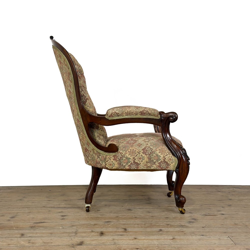 Victorian carved mahogany armchair with deep button-backed floral tapestry upholstery, curved armrests, and cabriole legs on brass castors. View VI