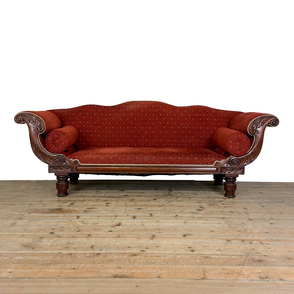 An antique Victorian walnut sofa with carved scroll arms, red patterned fabric upholstery, bolster cushions, and turned legs.