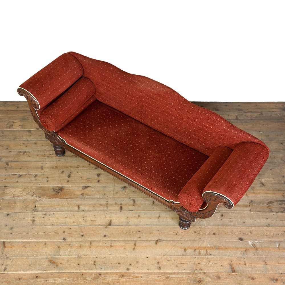 An antique Victorian walnut sofa with carved scroll arms, red patterned fabric upholstery, bolster cushions, and turned legs. View III