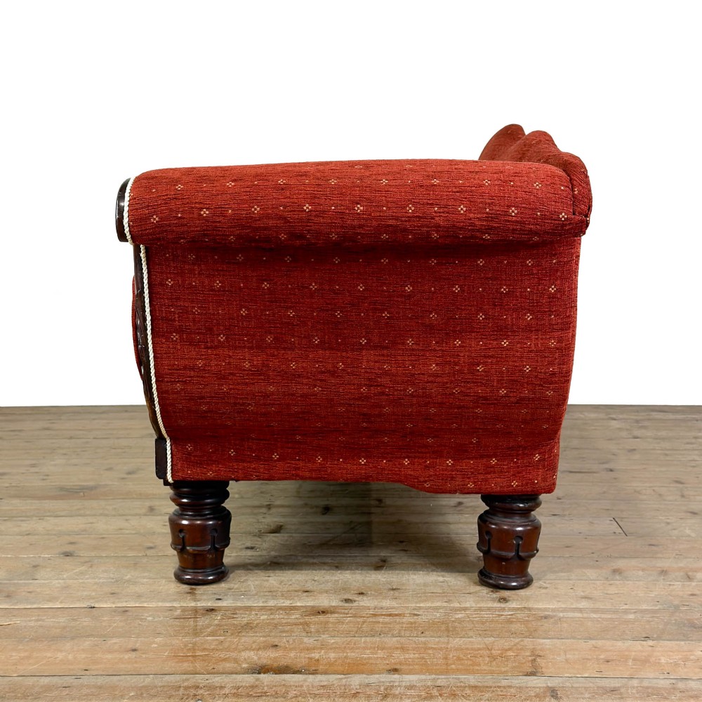 An antique Victorian walnut sofa with carved scroll arms, red patterned fabric upholstery, bolster cushions, and turned legs. View V