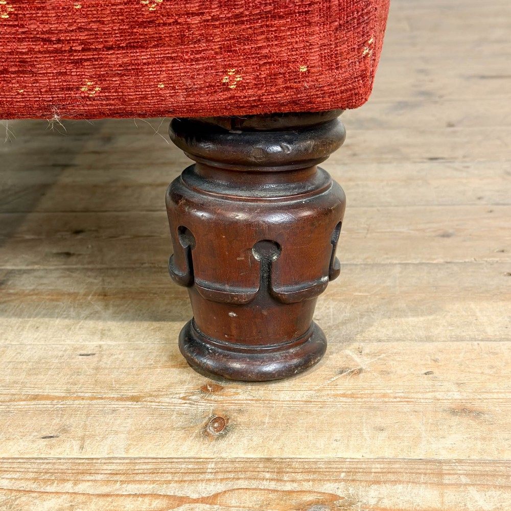 An antique Victorian walnut sofa with carved scroll arms, red patterned fabric upholstery, bolster cushions, and turned legs. View VI