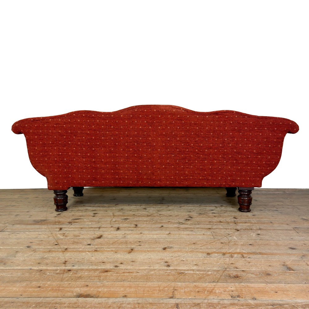 An antique Victorian walnut sofa with carved scroll arms, red patterned fabric upholstery, bolster cushions, and turned legs. View VII