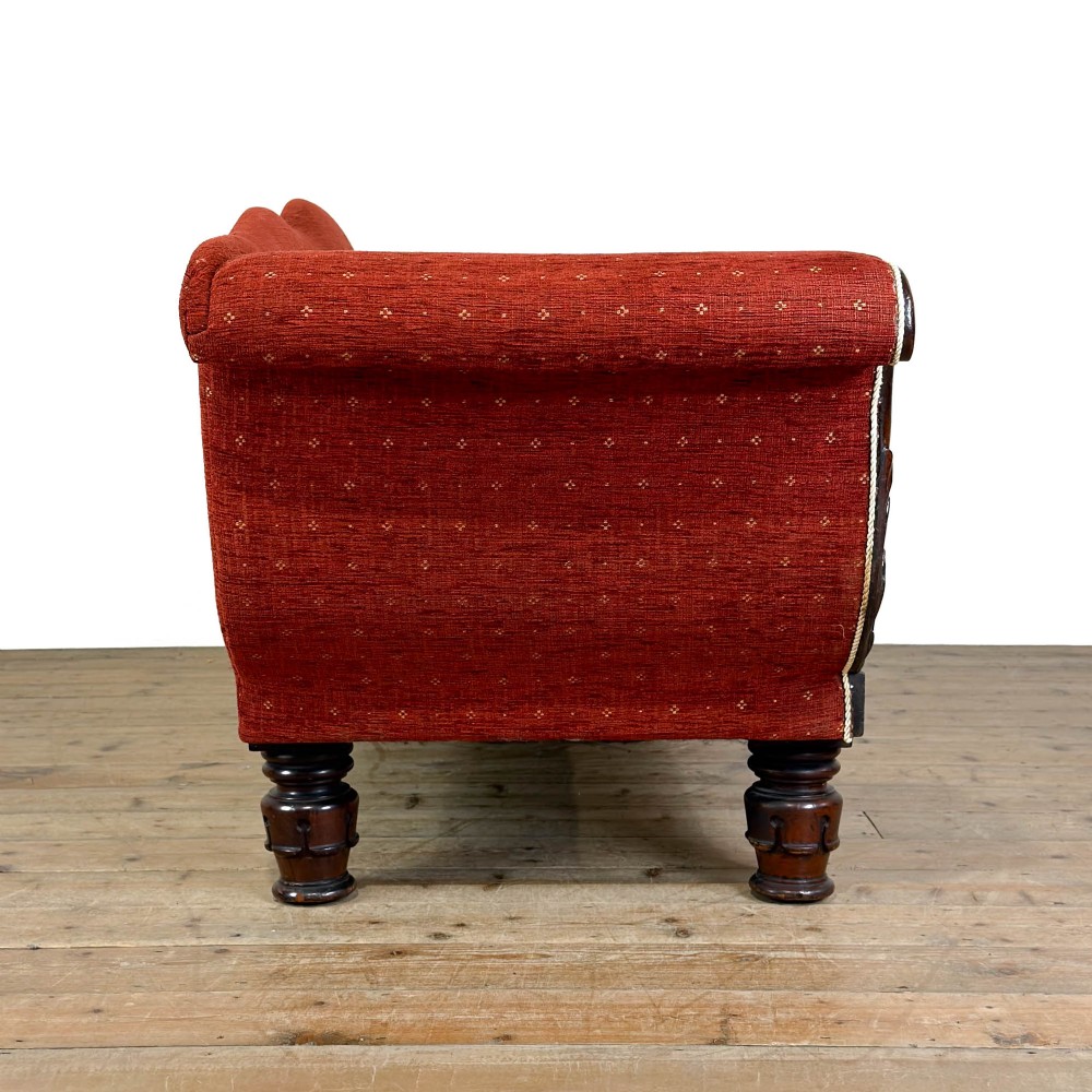 An antique Victorian walnut sofa with carved scroll arms, red patterned fabric upholstery, bolster cushions, and turned legs. View VIII