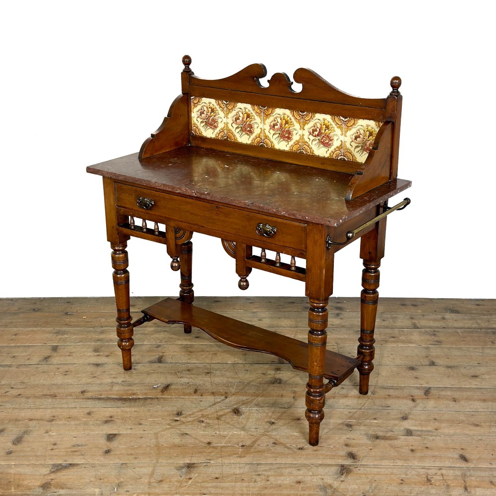 An Edwardian wooden washstand with a carved splashback housing floral glazed tiles, a single drawer with drop handles, turned legs, and an undertier shelf. View IV