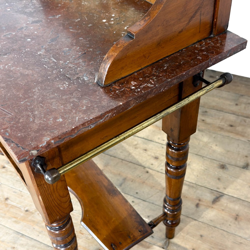 An Edwardian wooden washstand with a carved splashback housing floral glazed tiles, a single drawer with drop handles, turned legs, and an undertier shelf. View V