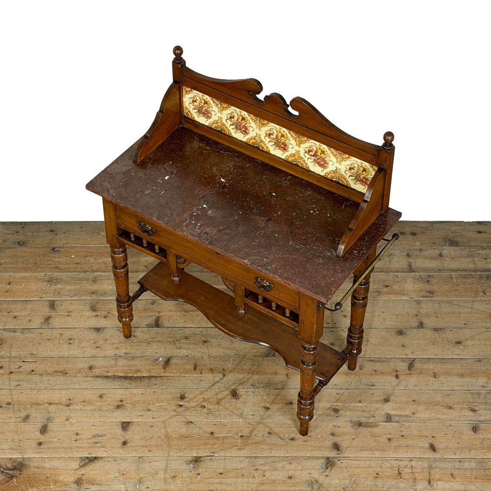 An Edwardian wooden washstand with a carved splashback housing floral glazed tiles, a single drawer with drop handles, turned legs, and an undertier shelf. View VI