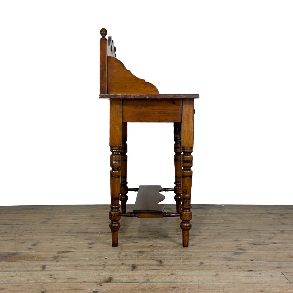 An Edwardian wooden washstand with a carved splashback housing floral glazed tiles, a single drawer with drop handles, turned legs, and an undertier shelf. View X