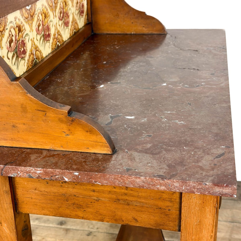 An Edwardian wooden washstand with a carved splashback housing floral glazed tiles, a single drawer with drop handles, turned legs, and an undertier shelf. View XI