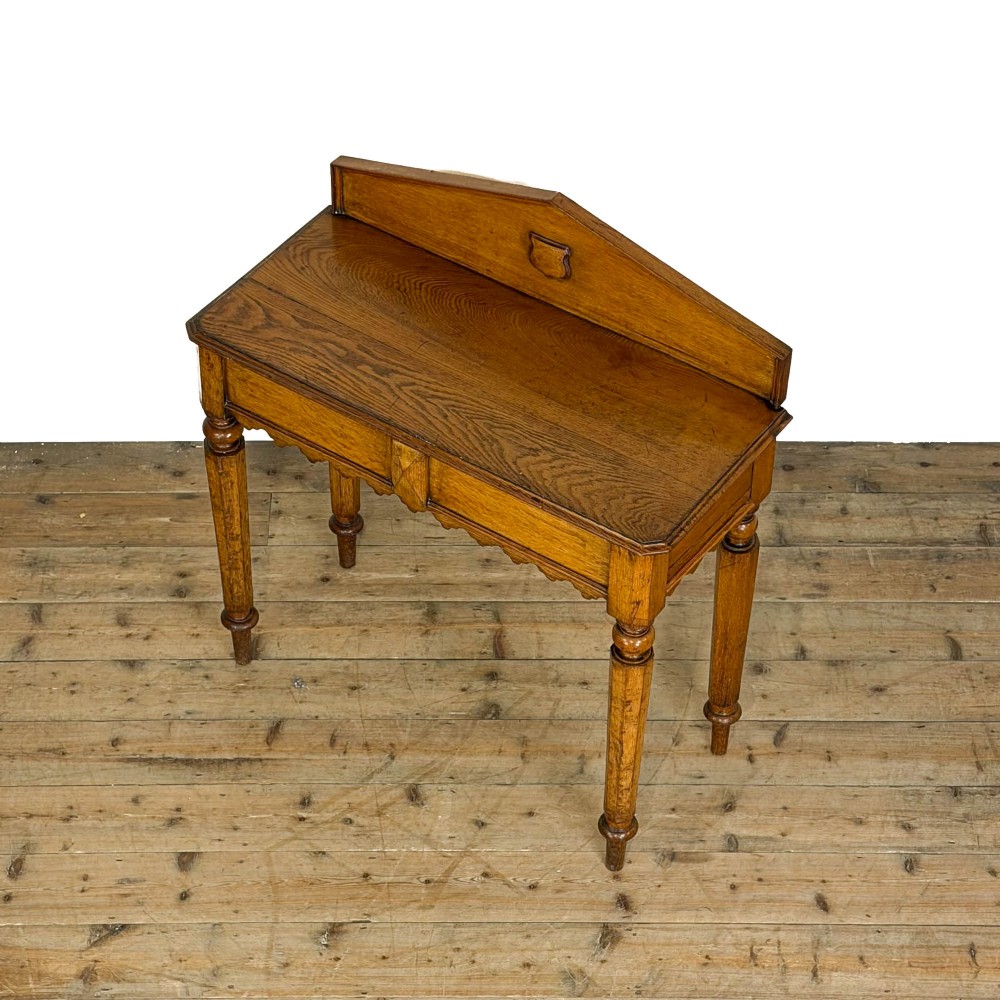 An antique warm brown oak hall table featuring a triangular gallery back with a central carved shield motif, a scalloped apron, and turned legs. View III
