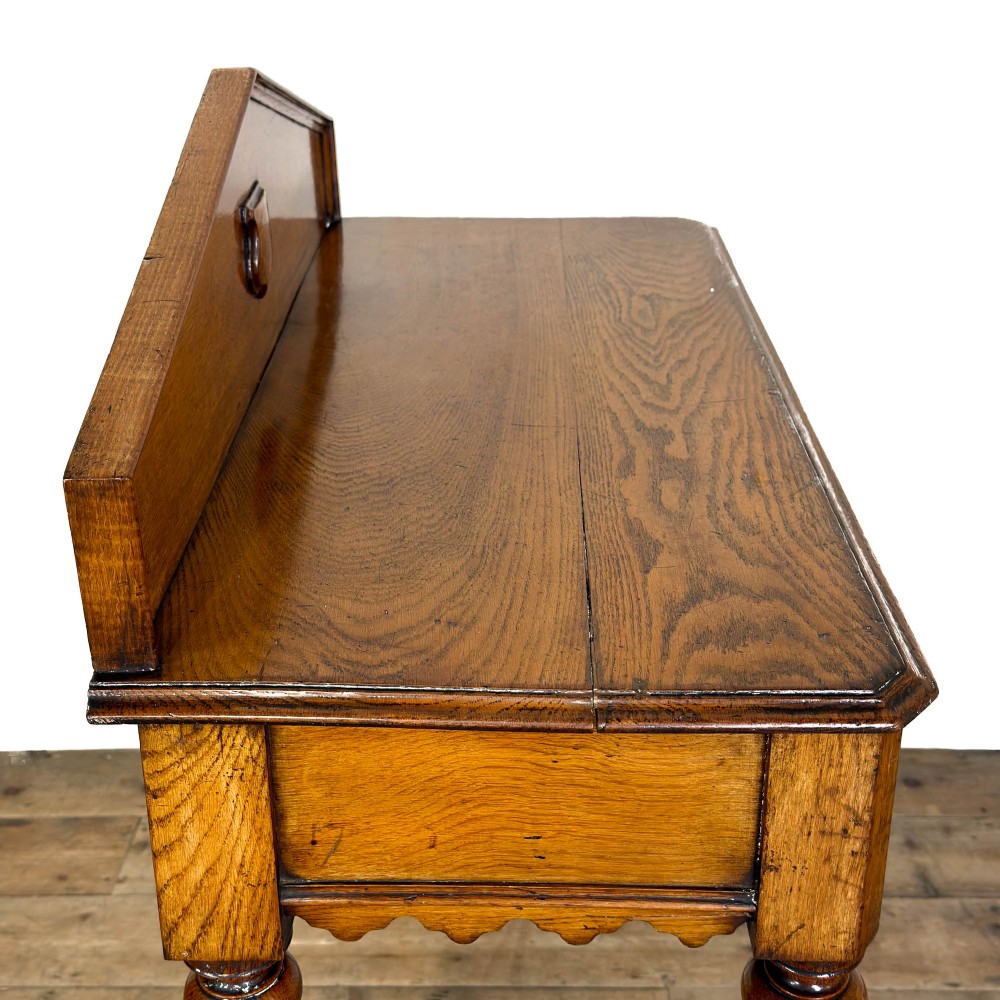 An antique warm brown oak hall table featuring a triangular gallery back with a central carved shield motif, a scalloped apron, and turned legs. View IV