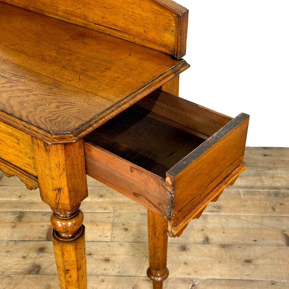 An antique warm brown oak hall table featuring a triangular gallery back with a central carved shield motif, a scalloped apron, and turned legs. View VI