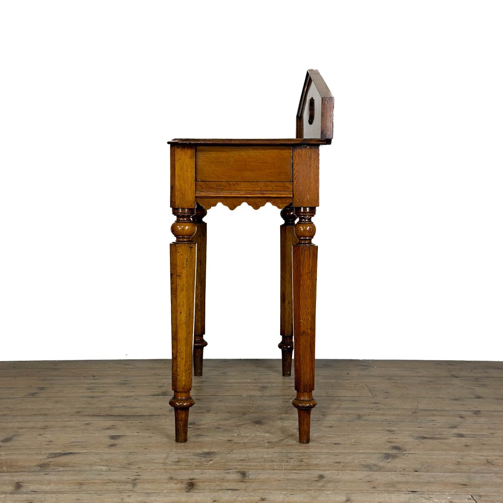 An antique warm brown oak hall table featuring a triangular gallery back with a central carved shield motif, a scalloped apron, and turned legs. View VII
