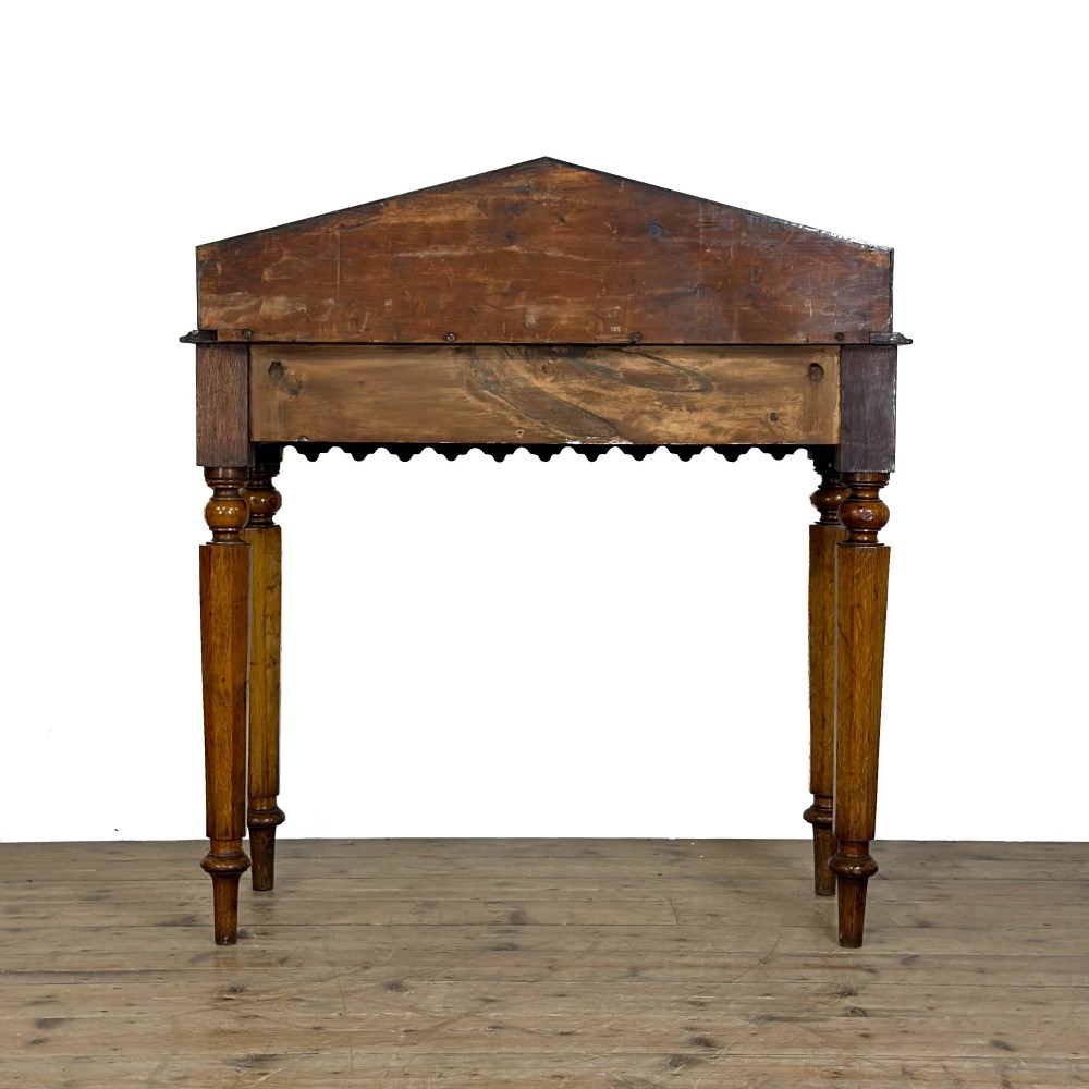 An antique warm brown oak hall table featuring a triangular gallery back with a central carved shield motif, a scalloped apron, and turned legs. View VIII