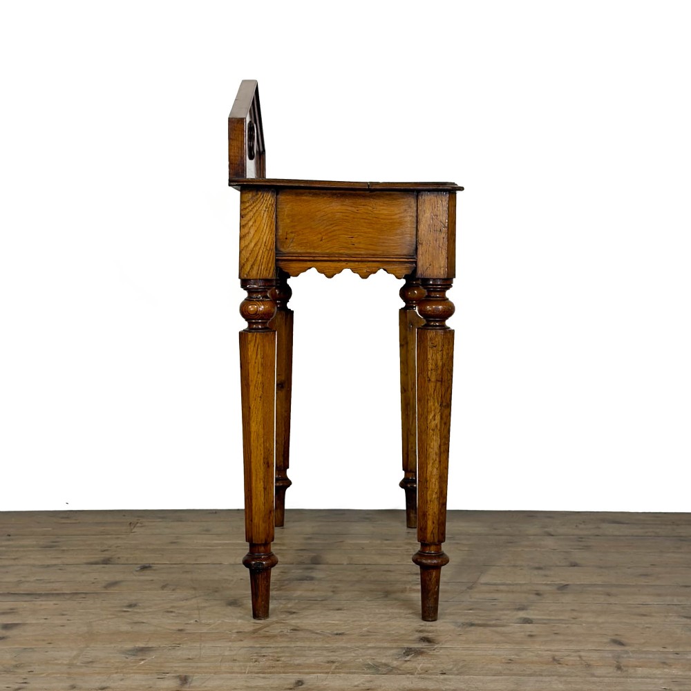 An antique warm brown oak hall table featuring a triangular gallery back with a central carved shield motif, a scalloped apron, and turned legs. View IX