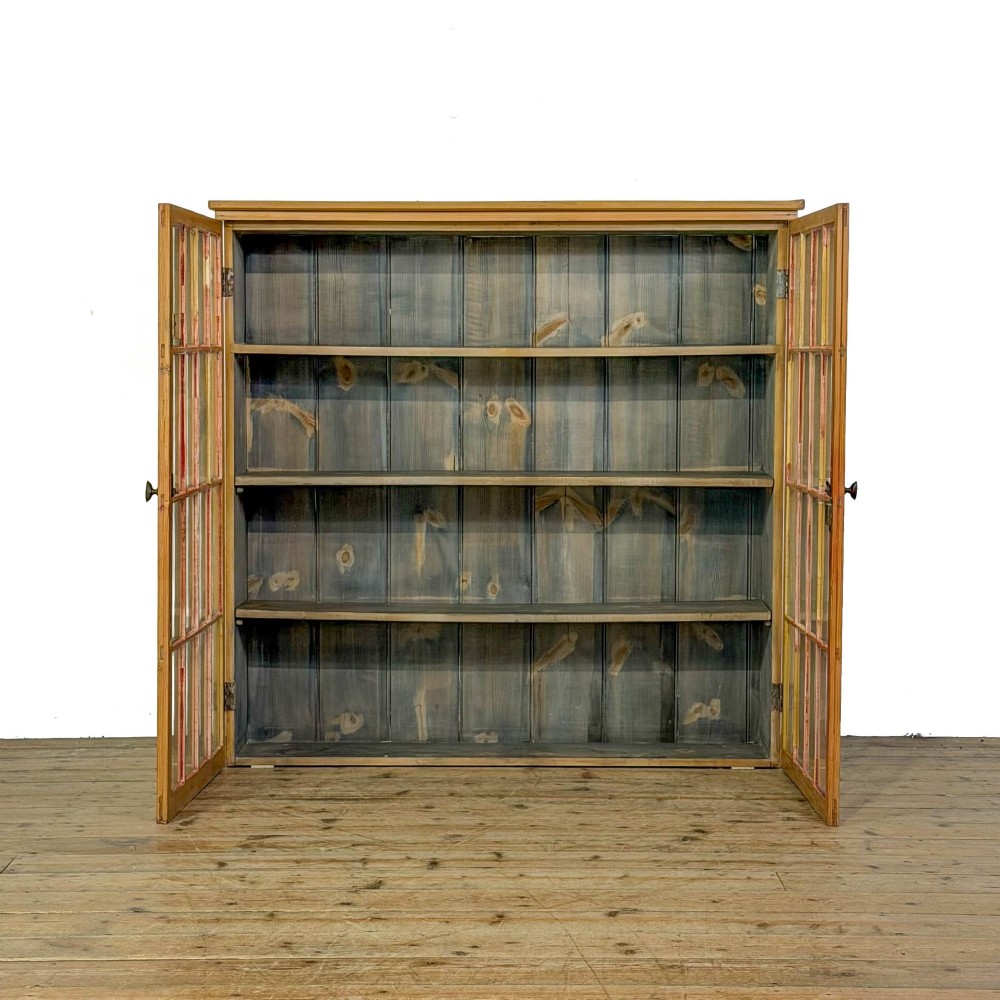 A large vintage pine cabinet featuring twin glazed doors with multiple glass panes and dark wooden knob handles. View III