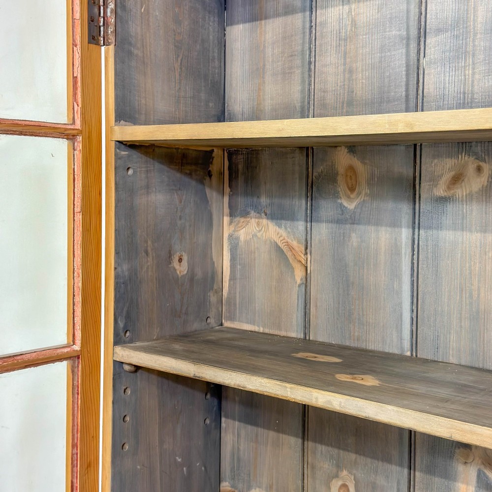 A large vintage pine cabinet featuring twin glazed doors with multiple glass panes and dark wooden knob handles. View IV