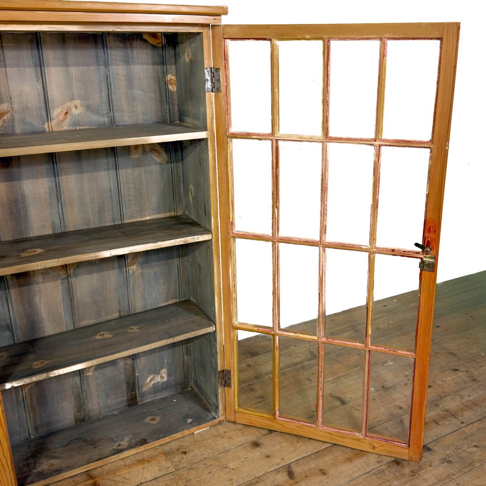 A large vintage pine cabinet featuring twin glazed doors with multiple glass panes and dark wooden knob handles. View V