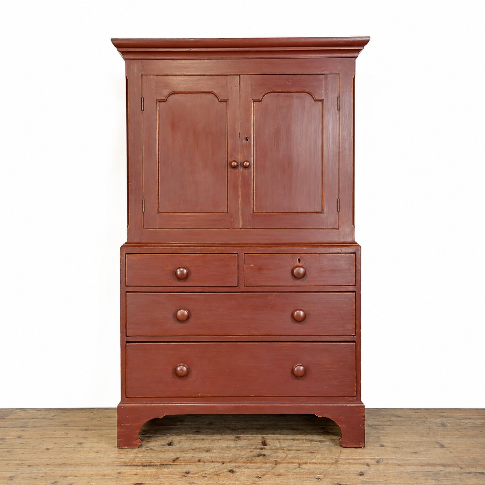 A tall Victorian painted pine housekeepers cupboard in a terracotta red finish, featuring a double-door upper cabinet over two short and two long drawers.