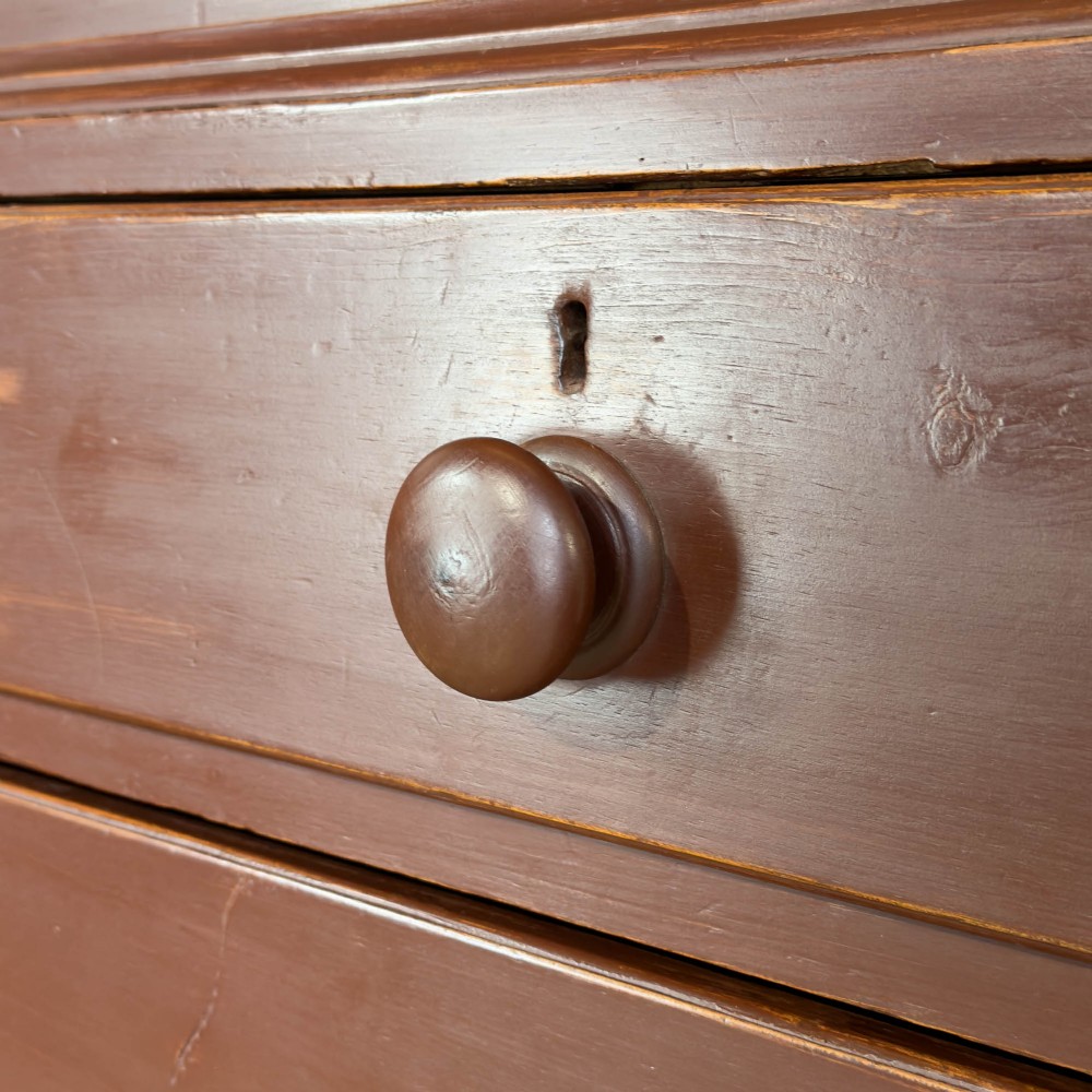 A tall Victorian painted pine housekeepers cupboard in a terracotta red finish, featuring a double-door upper cabinet over two short and two long drawers. View IV