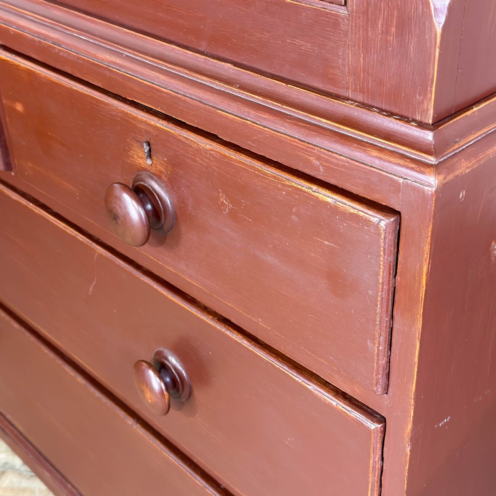 A tall Victorian painted pine housekeepers cupboard in a terracotta red finish, featuring a double-door upper cabinet over two short and two long drawers. View X