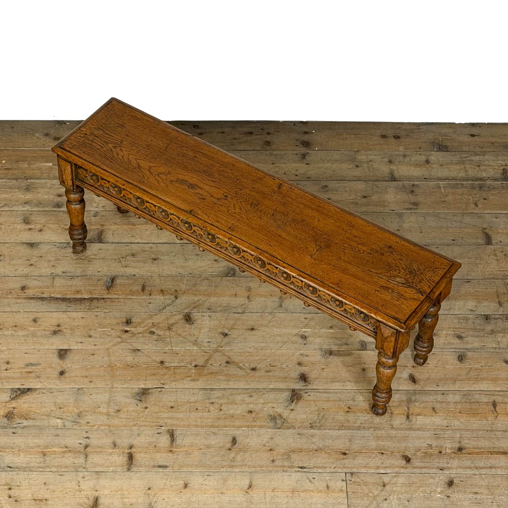 A long Victorian carved oak hall bench featuring a detailed floral rosette frieze, acorn drop pendants, and four turned legs on a light timber floor. View IV