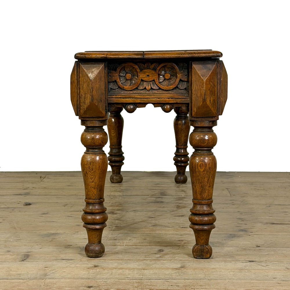 A long Victorian carved oak hall bench featuring a detailed floral rosette frieze, acorn drop pendants, and four turned legs on a light timber floor. View V
