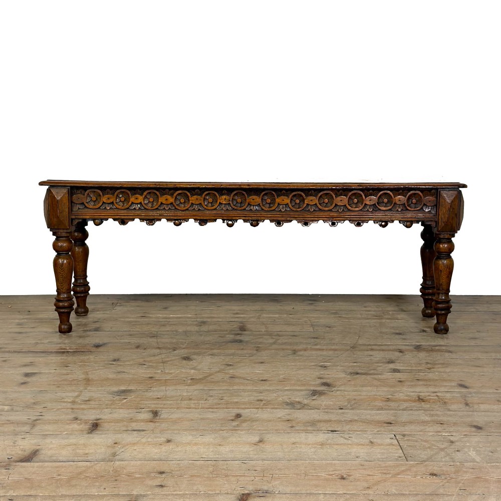 A long Victorian carved oak hall bench featuring a detailed floral rosette frieze, acorn drop pendants, and four turned legs on a light timber floor. View VI