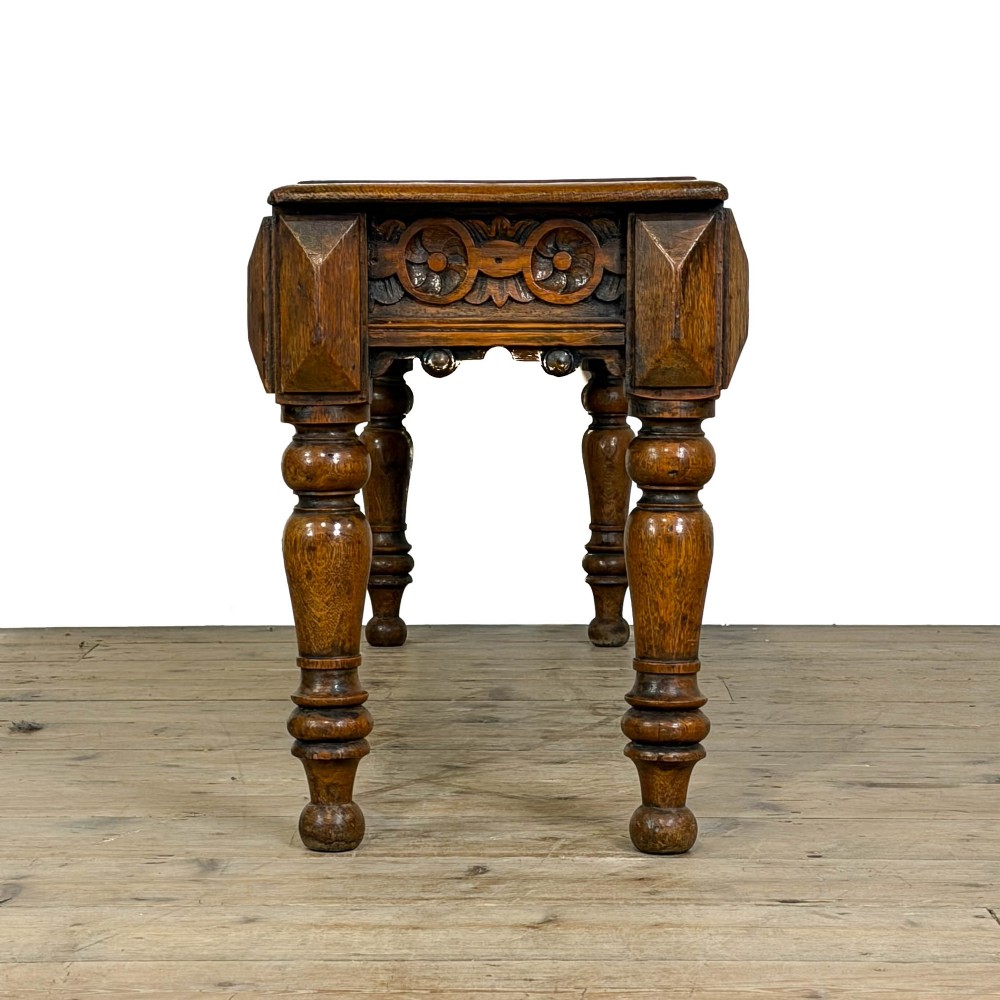 A long Victorian carved oak hall bench featuring a detailed floral rosette frieze, acorn drop pendants, and four turned legs on a light timber floor. View VII