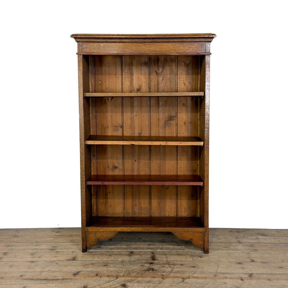 An open antique oak bookcase featuring four wooden shelves, a upper moulded cornice, vertical pine backboards, and shaped bracket feet.