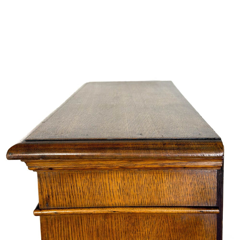 An open antique oak bookcase featuring four wooden shelves, a upper moulded cornice, vertical pine backboards, and shaped bracket feet. View IX
