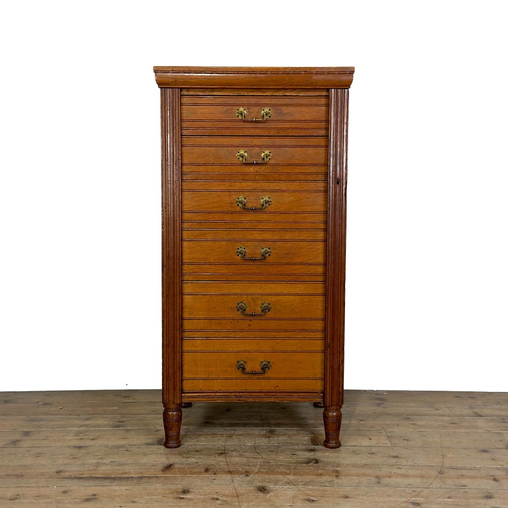 A tall late Victorian oak Wellington chest featuring seven drawers with brass drop handles, fluted side pilasters, and turned feet.