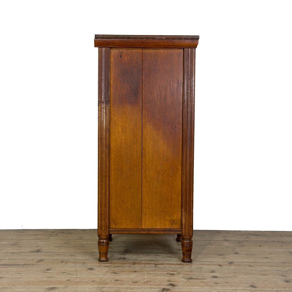 A tall late Victorian oak Wellington chest featuring seven drawers with brass drop handles, fluted side pilasters, and turned feet. View III