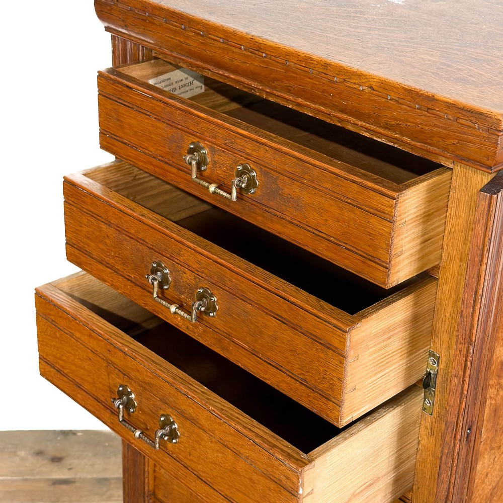 A tall late Victorian oak Wellington chest featuring seven drawers with brass drop handles, fluted side pilasters, and turned feet. View VI