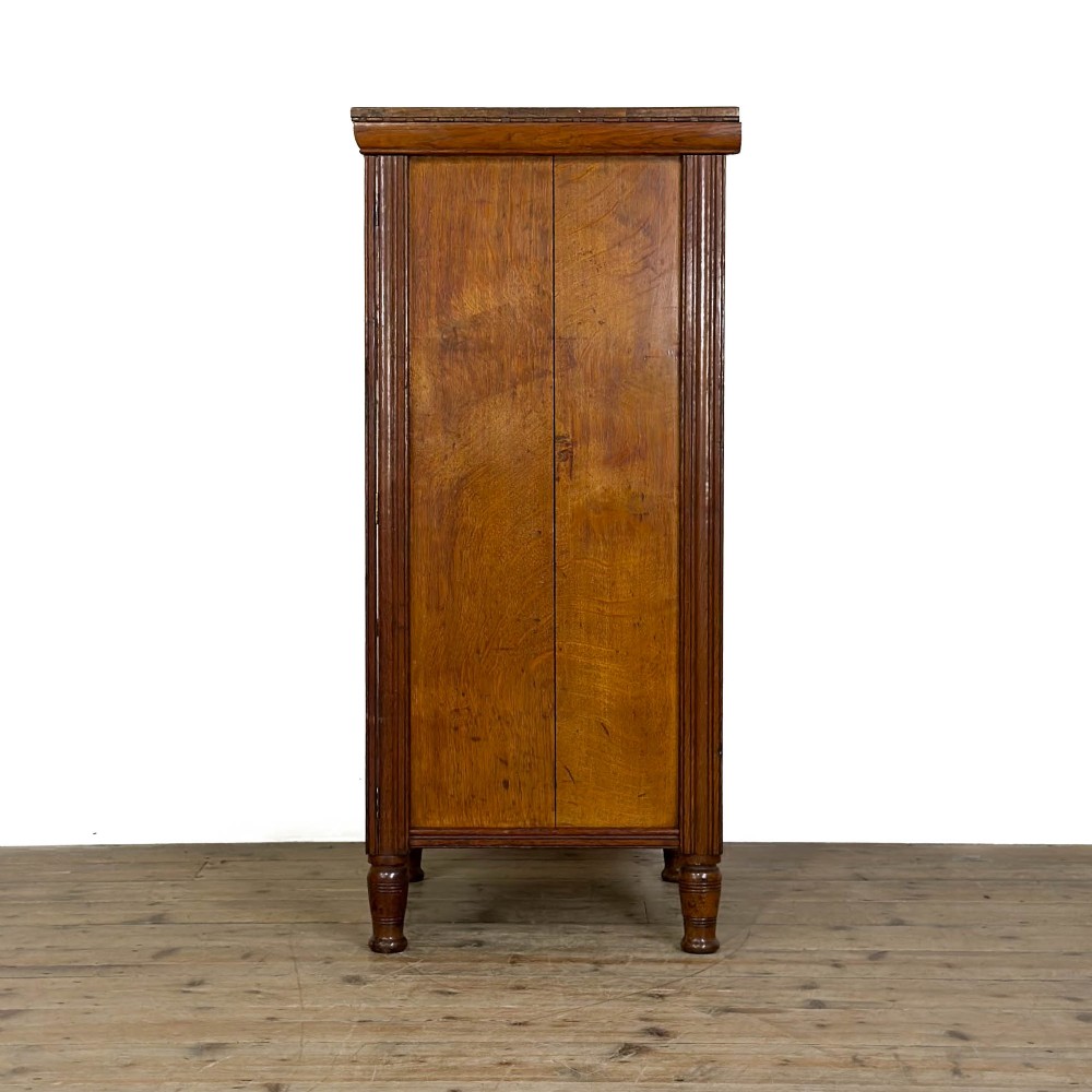 A tall late Victorian oak Wellington chest featuring seven drawers with brass drop handles, fluted side pilasters, and turned feet. View VIII