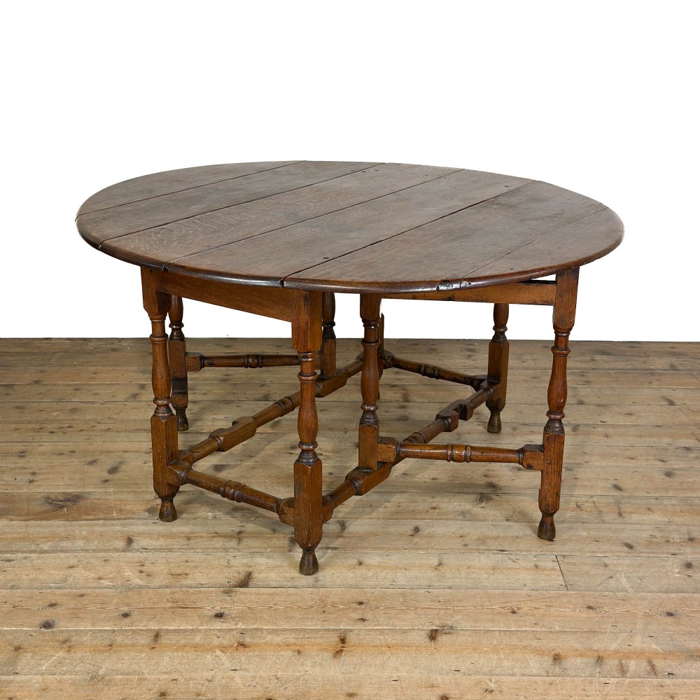 A warm brown oak gateleg dining table with raised drop leaves, turned leg supports, and lower box stretchers.