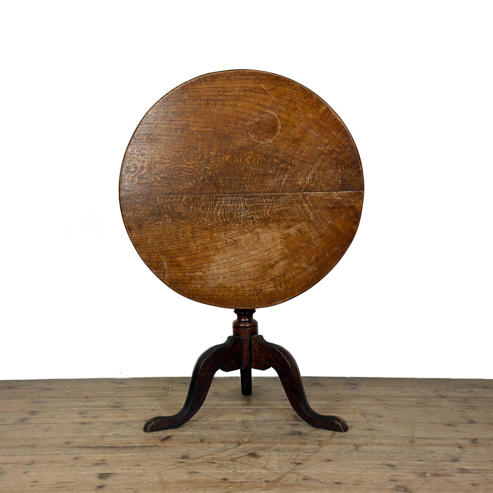 A Georgian oak tilt top table with a circular top locked upright above a turned column pedestal and three shaped tripod legs.