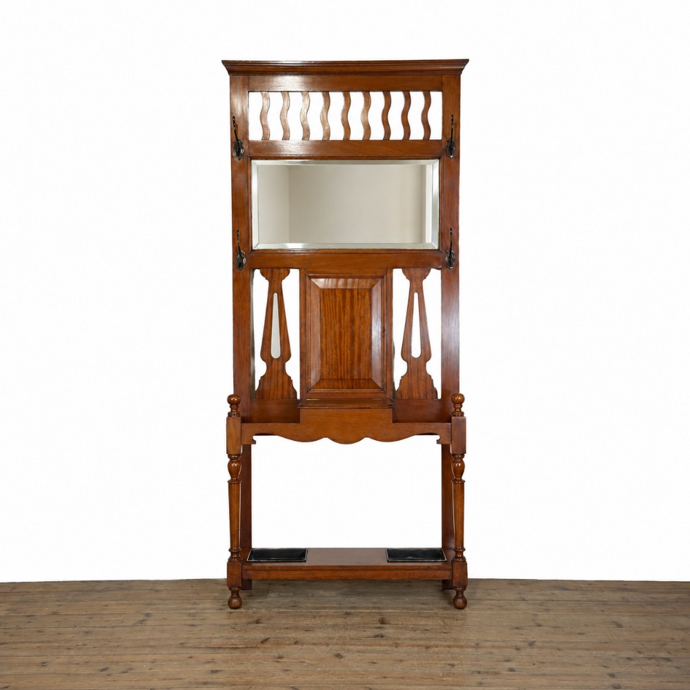 An antique Edwardian oak hall stand featuring a central mirror, hanging hooks, vertical spindle detailing, and a lower umbrella rack with drip trays.
