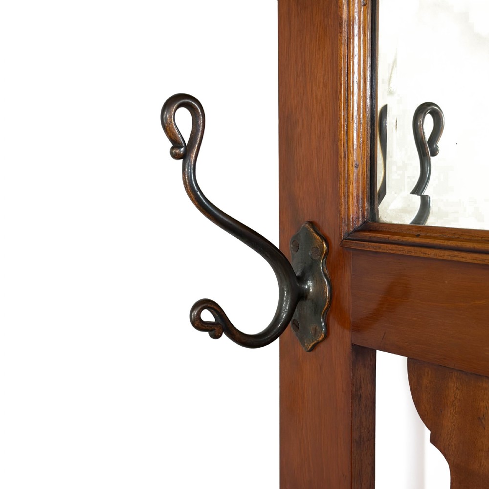 An antique Edwardian oak hall stand featuring a central mirror, hanging hooks, vertical spindle detailing, and a lower umbrella rack with drip trays. View V