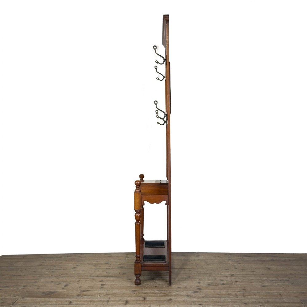 An antique Edwardian oak hall stand featuring a central mirror, hanging hooks, vertical spindle detailing, and a lower umbrella rack with drip trays. View VI