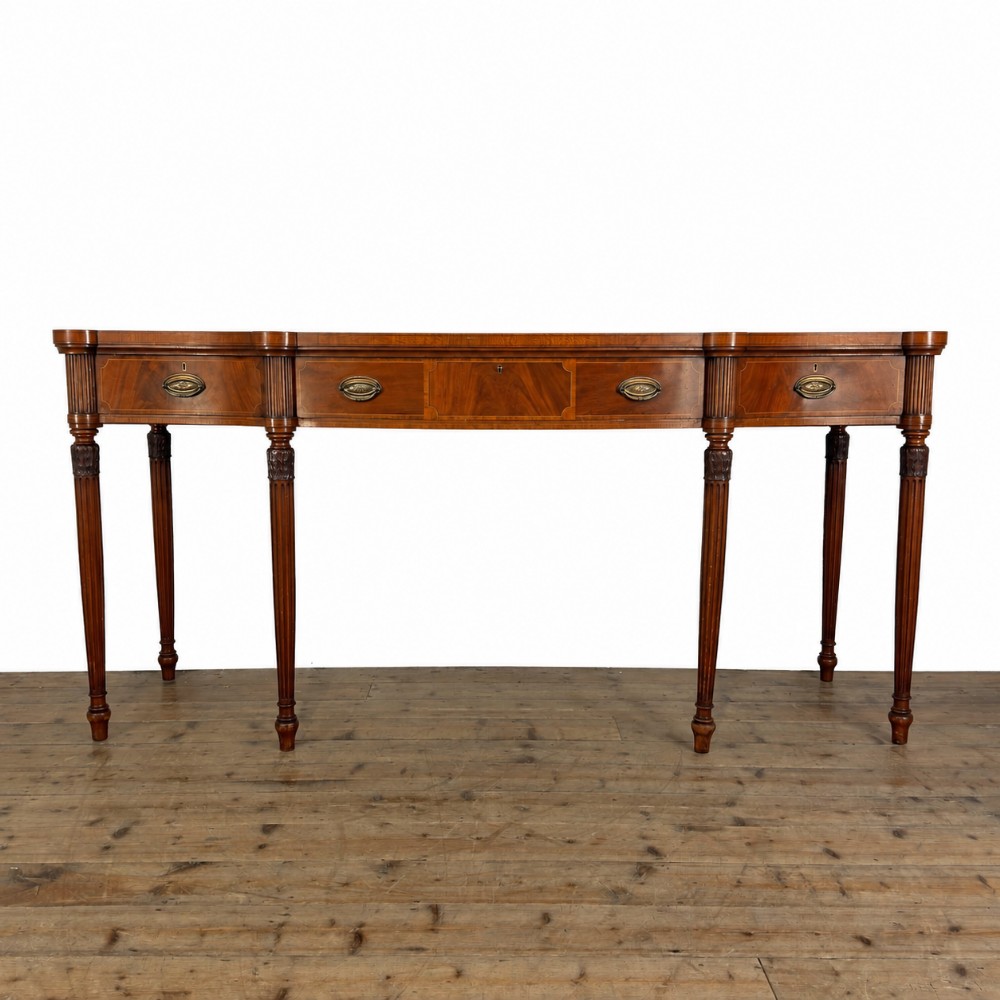 An Edwardian mahogany serving table featuring inlaid drawer fronts, brass oval handles, and slender fluted tapered legs.