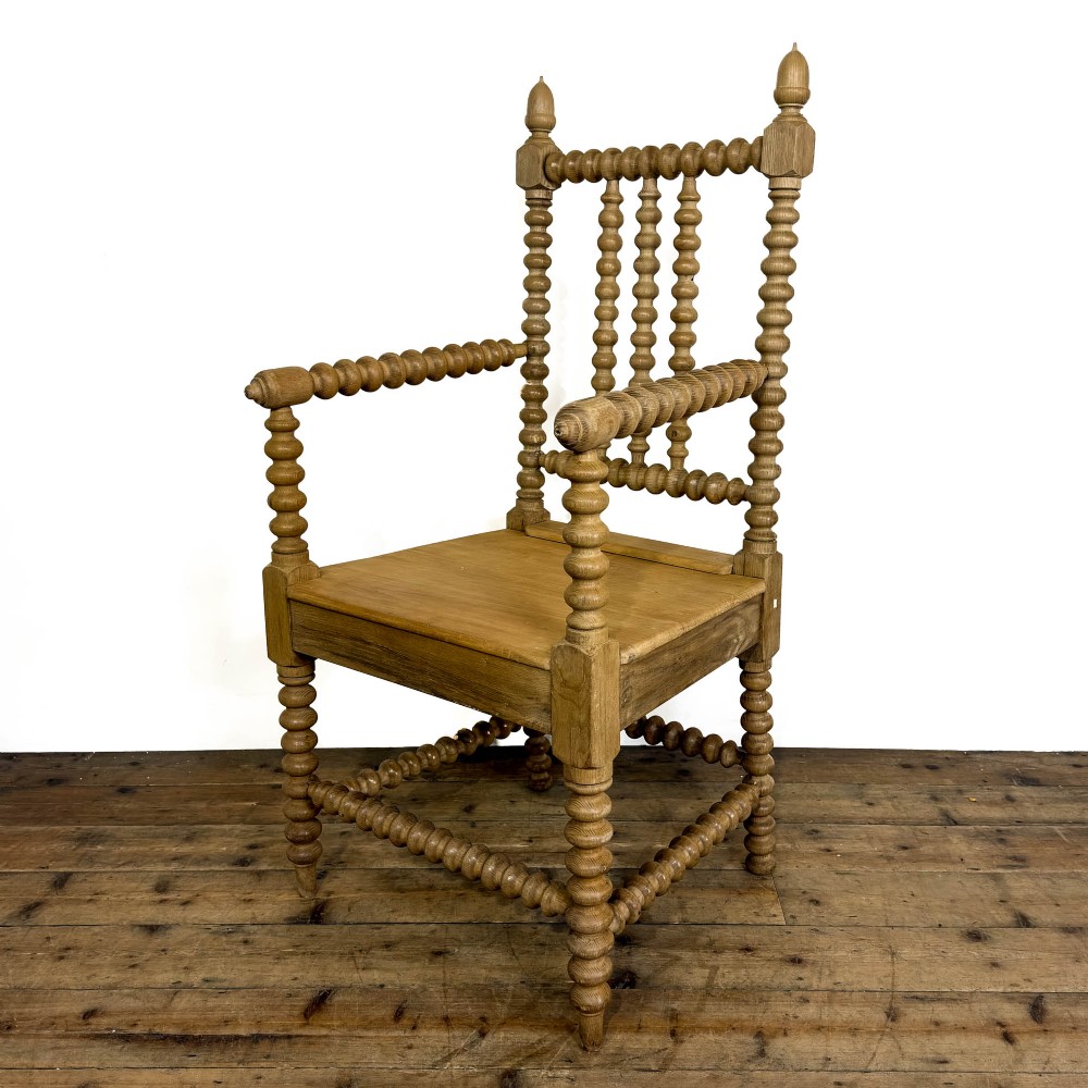 An antique light oak armchair constructed with lathe-turned bobbin spindles along the frame, backrest, armrests, and legs, topped with carved finials.
