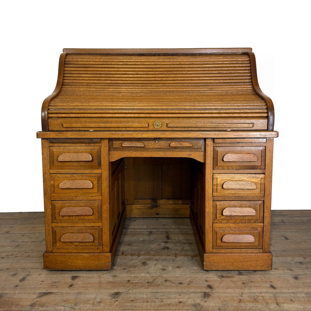 An antique golden oak roll-top desk with twin pedestals, multiple drawers, and wooden cup handles.