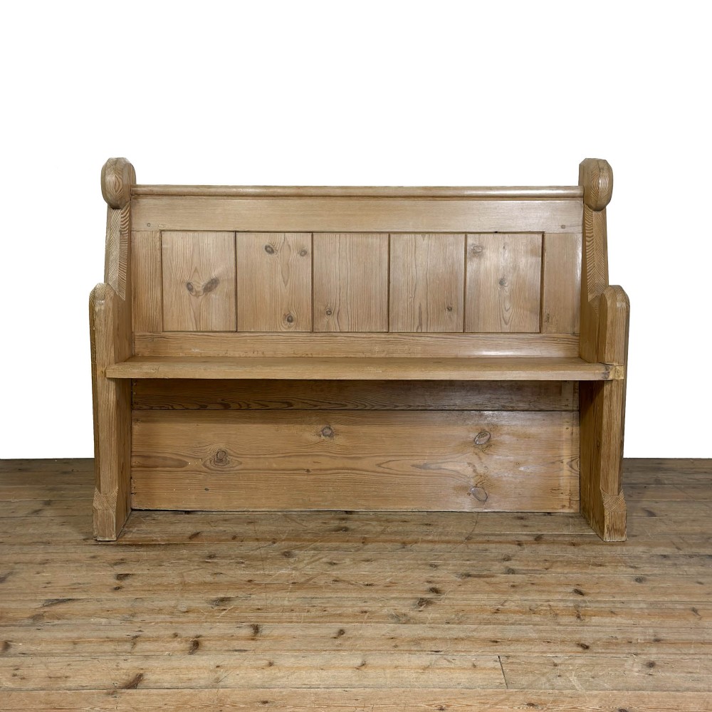 A freestanding antique pine chapel pew featuring a panelled backrest, solid bench seat, and carved upright side supports.