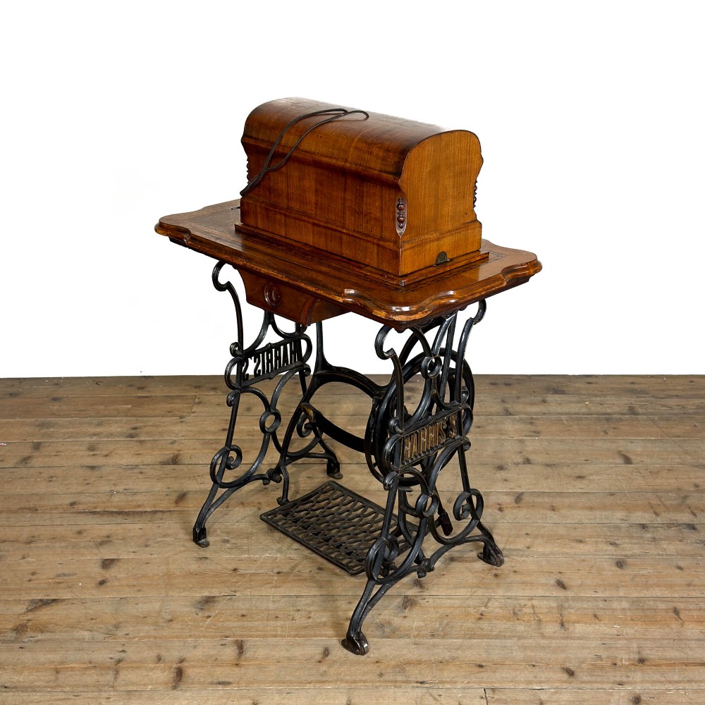 An antique Harris treadle sewing machine with a domed wooden case resting on an ornamental black cast iron treadle base.