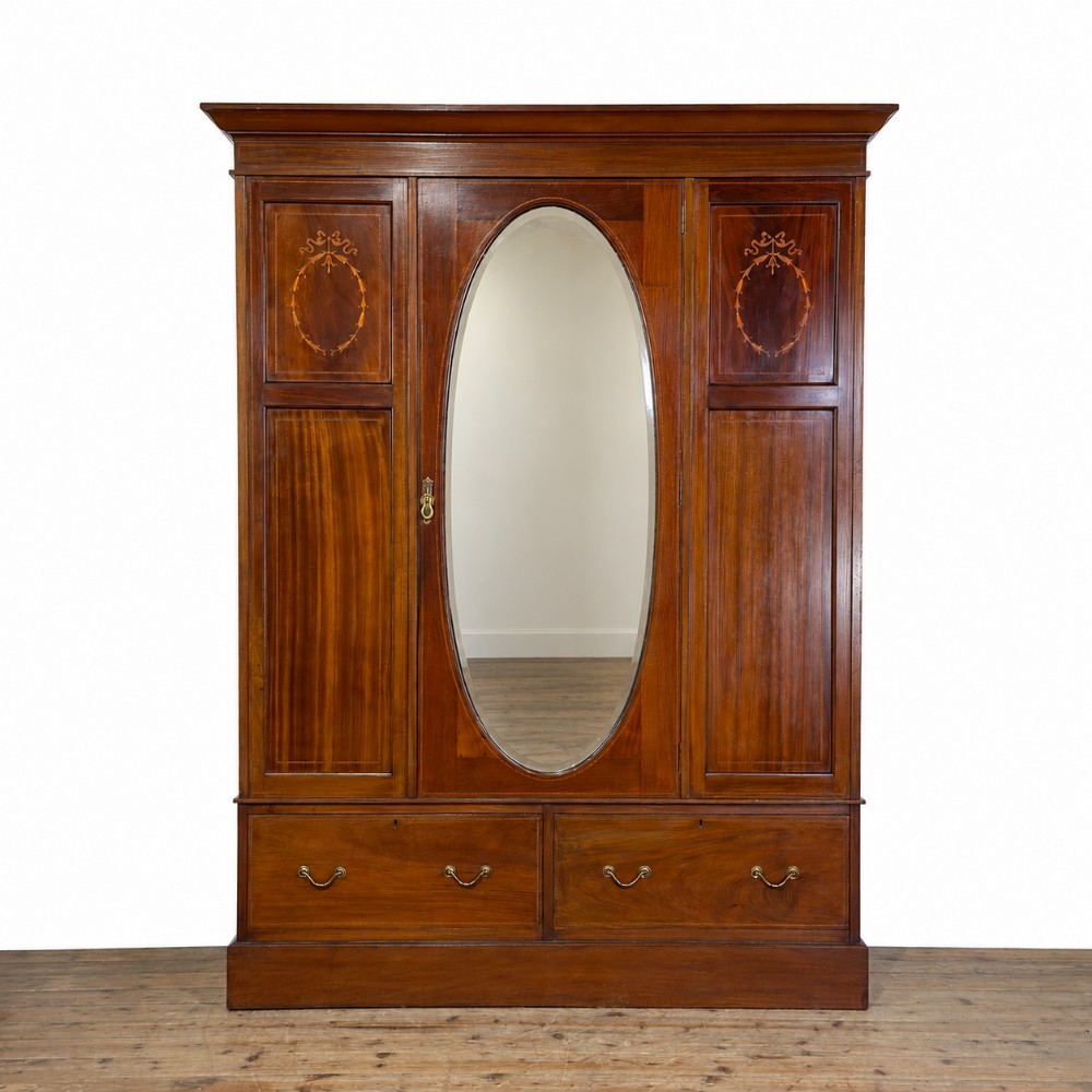 An Edwardian mahogany three-door wardrobe with a central oval bevelled mirror, delicate satinwood marquetry panels, and two lower drawers.