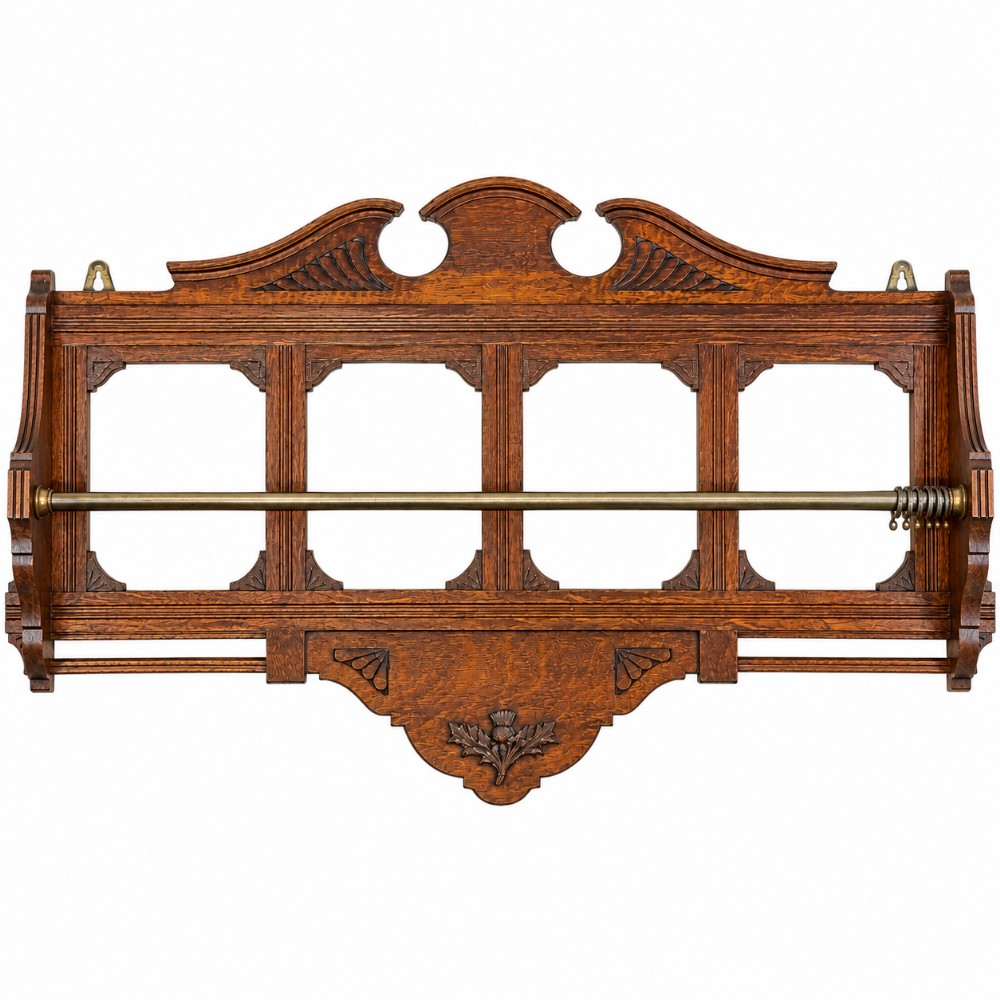 A Victorian carved oak wall rack featuring an architectural pediment, four open rectangular frame panels, a brass hanging rod with rings, and a carved Scottish thistle motif on the lower apron.