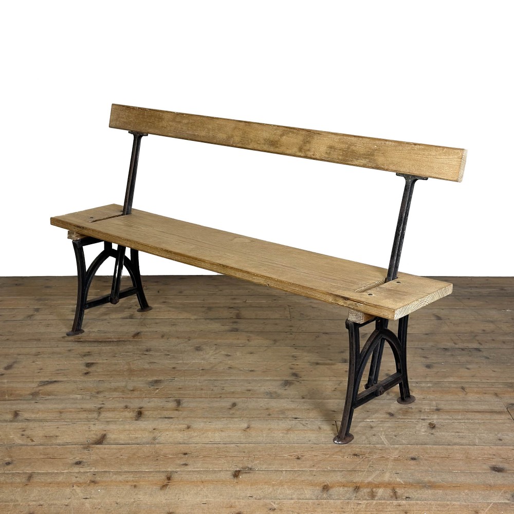 An antique pine bench featuring a reversible backrest supported on dark cast iron legs.
